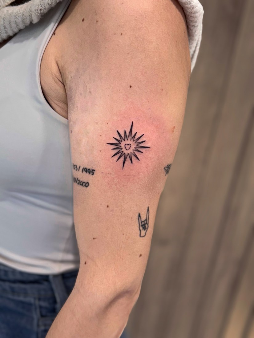 Tatuaje fine line de un sol con un corazón en el brazo